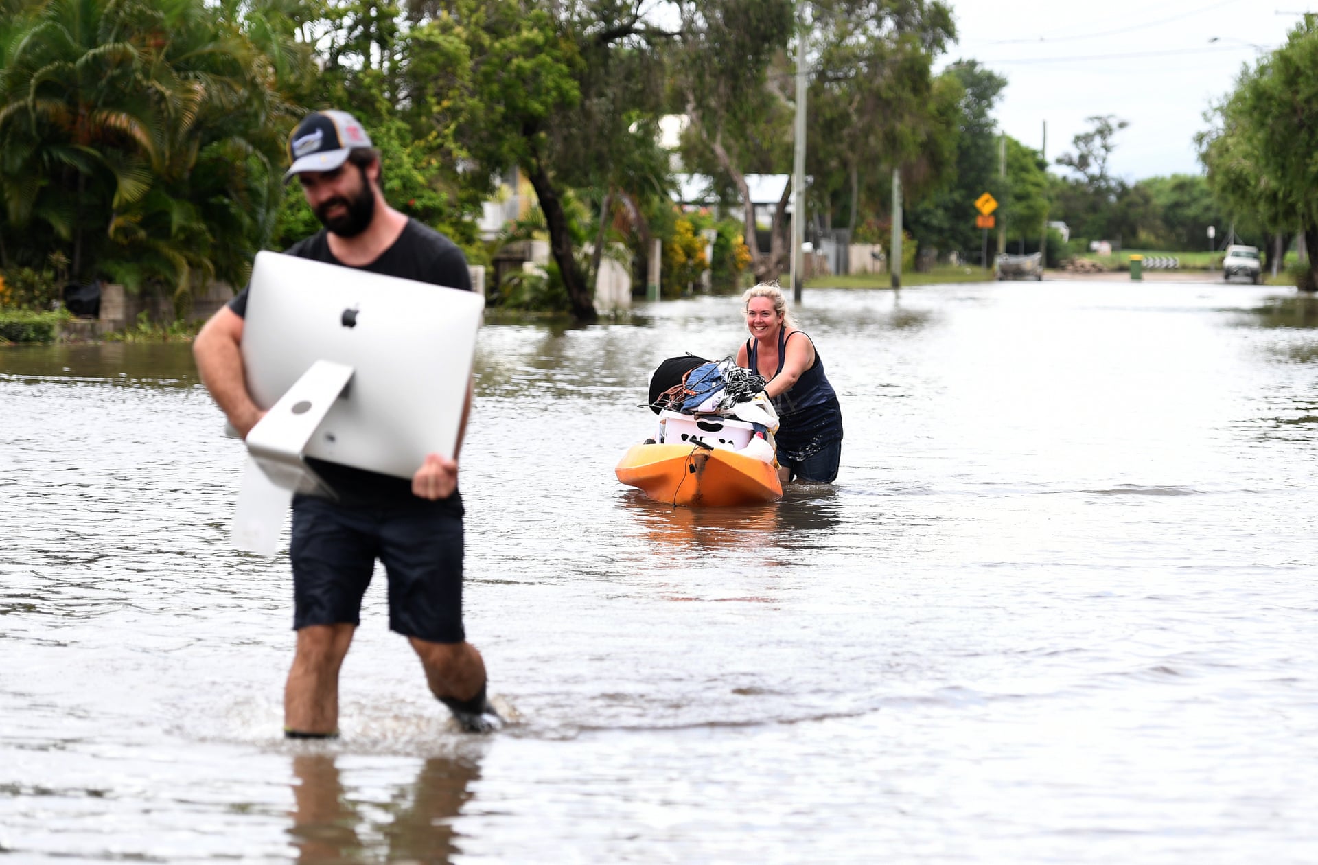 A man hugs his iMac as he makes his way through a flooded street, a woman pushes a kayak packed with the rest of their belongings.